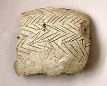 Photographie en gros plan d'un tesson de poterie sur lequel sont gravé des lignes parallèles en chevrons.