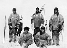 Пятеро мужчин в тяжелой полярной одежде. Все выглядят недовольными. Стоящие люди несут флагштоки, на мачте на заднем плане развевается флаг Союза.
