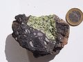 Peridotit (lục) trong bom núi lửa ở Vulkan-Eifel, Đức. Đồng xu là 1 euro làm thước tỉ lệ.