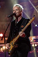 A Caucasian man is singing while playing on a guitar