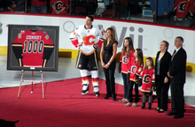 a man is pictured alongside his wife and three daughters as he is presented with a framed hockey jersey with the numeber 1000 on its back.