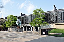 a low steel and glass building and concrete courtyard, with the words Paul V. Galvin Library about a bank of doors, flanked by trees and an abstract steel sculpture