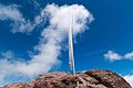 Photo couleur d'une lame de sabre enchâssée dans une roche sur fond de ciel bleu nuageux.