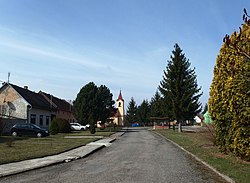 Podlouhlá náves se středním pásem zeleně, kaplí a autobusovou zastávkou