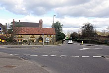 mini-roundabout beside a long, low, 2-storey stone cottage with yellow-painted window frames