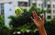 photo d'une balle de tennis mouillée tourbillonant ; les gouttes d'eau s'en détachent en arcs divergents