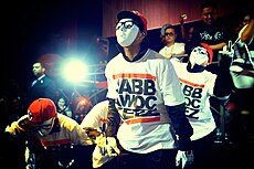 Четыре члена танцевальной хип-хоп команды JabbaWockeeZ выступают в ночном клубе в белых масках и белых перчатках.