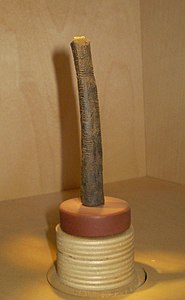 Longo osso castanho (a fíbula de um babuíno) com um pedaço de quartzo afiado incrustado em uma ponta, possuindo uma série de traços talhados, divididos em três colunas, ao longo de todo o comprimento.