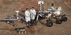 Two Jet Propulsion Laboratory engineers stand with three vehicles, providing a size comparison of three generations of Mars rovers. Front and center left is the flight spare for the first Mars rover, Sojourner, which landed on Mars in 1997 as part of the Mars Pathfinder Project. On the left is a Mars Exploration Rover (MER) test vehicle that is a working sibling to Spirit and Opportunity, which landed on Mars in 2004. On the right is a test rover for the Mars Science Laboratory, which landed as Curiosity on Mars in 2012.
Sojourner is 65 cm (26 in) long. The Mars Exploration Rovers (MER) are 1.6 m (5 ft 3 in) long. Curiosity on the right is 3 m (9.8 ft) long. PIA15279 3rovers-stand D2011 1215 D521.jpg