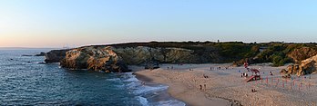 Praia Grande ao entardecer. Porto Covo, Portugal. Embora caracterizada como uma “pequena comunidade de pescadores”, seu movimento em direção ao mercado turístico tem impulsionado seu crescimento desde a década de 1990. Influenciada por suas praias de areia branca e fina, costões naturais de rochas, enseadas isoladas e temperaturas amenas, a economia local absorve um número constante de visitantes de verão e turistas estrangeiros. Em frente à ilha do Pessegueiro está uma das praias mais populares, atraindo windsurfistas, velejadores e pescadores esportivos para as águas da costa. (definição 12 020 × 4 042)