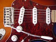 Detail of a Squier-made Fender Stratocaster. Note the tremolo arm, the 3 single-coil pickups, the volume and tone knobs.