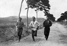 Trois hommes en habits amples et en pleine course sur une route de campagne.