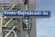 Blaues Straßennamensschild mit weißer Schrift "Centa-Hafenbrädl-Str." vor einem Rohbau mit Gerüst.