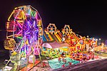 Illuminated Ferris wheel, bouncing castle and carousel at night in a funfair in Vientiane, Laos.jpg