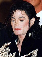 Close-up of a pale skinned Jackson with black hair. He is wearing a black jacket with white designs on it.