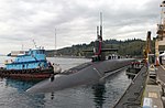 Submarine being assisted into a mooring position at a pier by a tug.