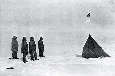冰天雪地中，四個身穿厚重棉襖的人站在左側，右側是一個深色的帳篷，由若干繩索固定，帳篷上插著兩面旗幟，上方是挪威國旗，下方是前進號船旗。