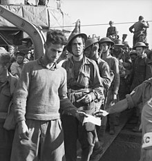 Uma fila de soldados desarmados desembarcando de um navio por um corredor.