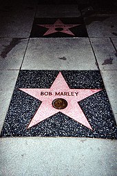 A five pointed pink star inlaid in the sidewalk with Bob Marley written on it.