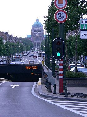 Boulevard arboré à 4 voies avec entrée d'un tunnel et feu vert au premier plan et la basilique au fond