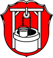Gemeinde Waldbüttelbrunn In Rot ein silberner Ziehbrunnen mit Eimer an der Kette.