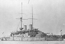 Grey warship with low deck and high superstructure, and barbette armament