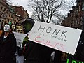 A protester dressed as "Anonymous" encourages people to honk their horns