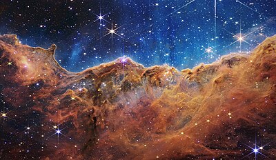 Gas yang terdorong oleh radiasi ultraviolet intens dari pembentukan bintang-bintang baru di bagian barat gugus bintang terbuka NGC 3324, sekitar 7.600 tahun cahaya dari Bumi, di rasi bintang Carina yang diamati dari Teleskop Luar Angkasa James Webb pada 12 Juli 2022. Radiasi yang sangat kuat dari bintang-bintang baru ini "memahat" gas yang terdorong menyerupai tebing dan pegunungan di luar angkasa.