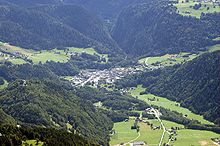 photographie couleur montrant une vue aérienne de Beaufort-sur-Doron, capitale du fromage de Beaufort. Le village paraît minuscule au fond de la vallée, écrasé par la forêt de sapins qui domine les reliefs les plus pentus. Les zones plus planes, des pâturages ou zones à fourrage donnent un peu de douceur au paysage.