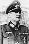 A man wearing a military uniform, peaked cap and neck order in the shape of a cross.