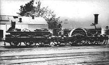 Черно-белое изображение, показывающее паровоз, повернутый вправо. У нижнего тендера слева шесть колес; у самого двигателя есть большое колесо посередине с двумя колесами спереди и одним сзади.