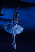 A ballerina in a white tutu, posing en point on a dimly lit stage