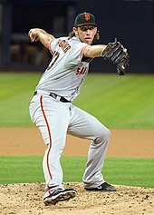 An action photograph of a baseball player pitching a baseball.