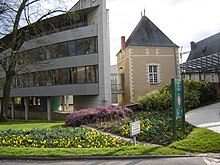 Photographie présentant le bâtiment de la mairie : à gauche, la partie moderne, sur pieux, raccordée à un bâtiment carré au centre par une passerelle vitrée, à droite la structure métallique qui abrite le cloitre d'eau.