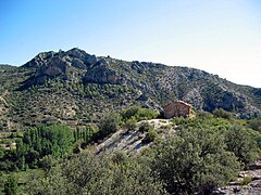 Vista general de la ermita de San Pedro de El Cuervo (Teruel), con la peña de Los Picarzos al fondo.