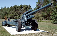 a shield-less mid-green artillery piece sitting on a concrete slab