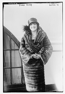 A smiling young white woman wearing a hat and a fur coat, photographed outdoors