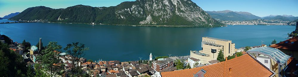 Het Meer van Lugano gezien vanaf Campione d'Italia; rechts op de voorgrond het casino; op de achtergrond rechts ligt Lugano; uiterst links is de dam bij Melide zichtbaar.