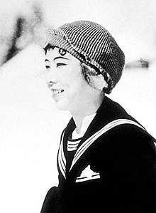 A young Japanese woman smiling outdoors, wearing a knit cap and a sailor-style pullover