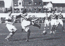 Photo en plein match. Sous le regard de ses coéquipiers et d'un adversaire, un joueur frappe dans la balle.