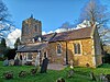 A stone church seen from the southeast with a south porch and a battlemented tower with a spirelet and weathervane