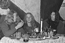 Black & white photo of Randy Holden (right), Paul Whaley (center), and Dickie Peterson (left) seated at a small dining table (left)