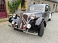 Une Citroën Traction 11 BL (Berline Légère) des années 1950, dans une belle et rutilante livrée grise métallisée avec les ailes noires.