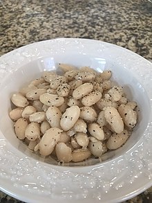 A bowl of cooked white beans garnished with olive oil and ground pepper