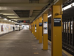 An underground train station with outer platforms. A pillar bisecting the image is painted a burnt yellow.