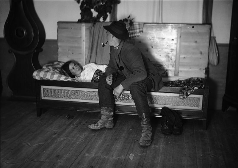 Nattfrieri. En man sitter på sängkanten och pratar med liggande kvinna. Värmland, Mangskogs socken. (public domain)
