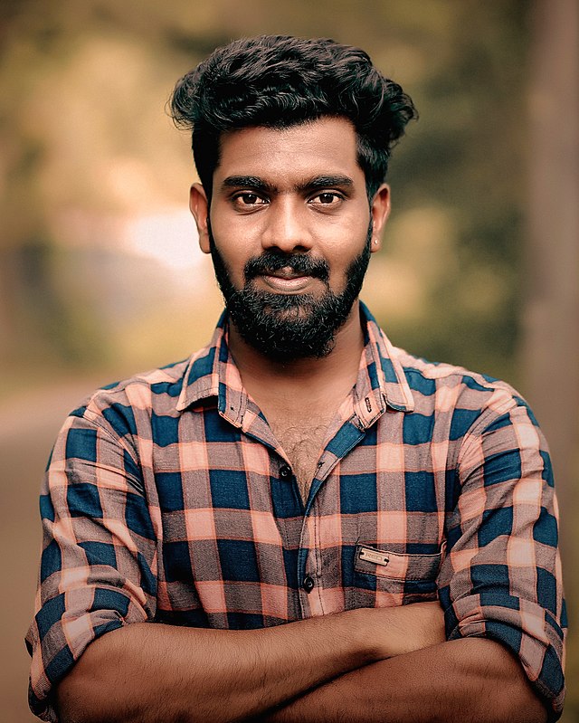 A man with a beard, wearing a checkered shirt, with his arms crossed.