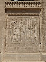 Ανάγλυφο σε screen wall μεταξύ στηλών σbetween columns at Dendera, with images of marsh plants at the base, torus moldings framing the relief, and a cavetto cornice with a winged sun emblem topped by a frieze of uraei. First to second century AD.[106]