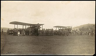 Two biplanes in a field surrounded by a crowd