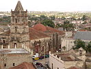 A view of a cityscape, dominated by what appears to be a place of worship, with a tower at one end, and a dome-shaped roof at the other. The building appears to be in a state of disrepair.